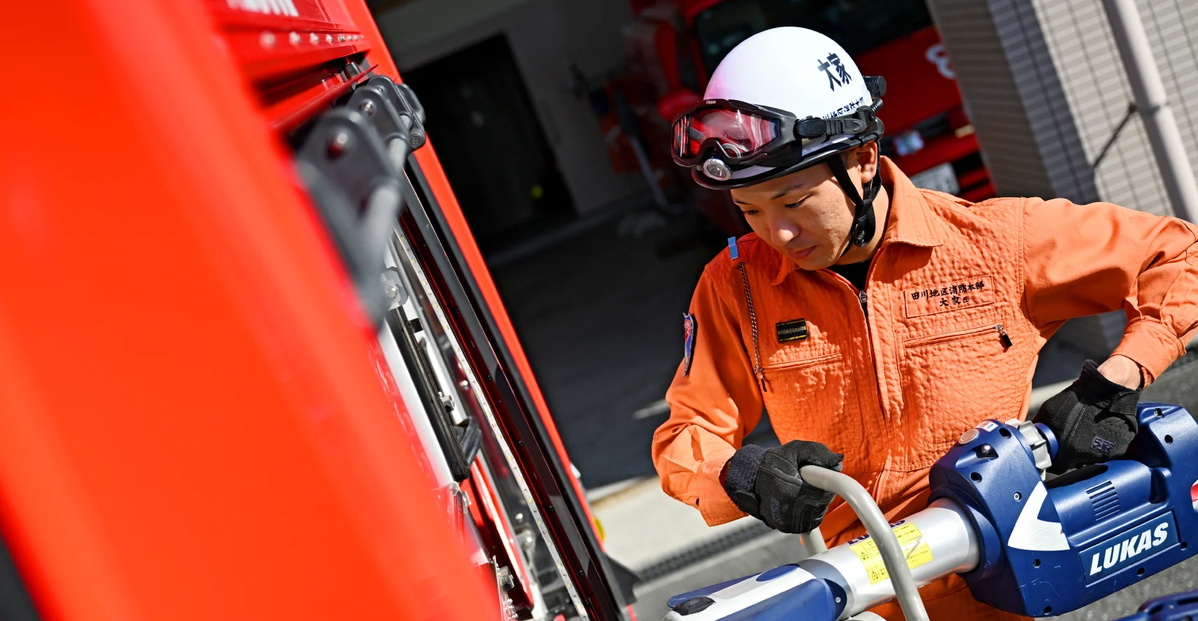大家さんが消防車からLUKASと書かれた道具を取り出している様子