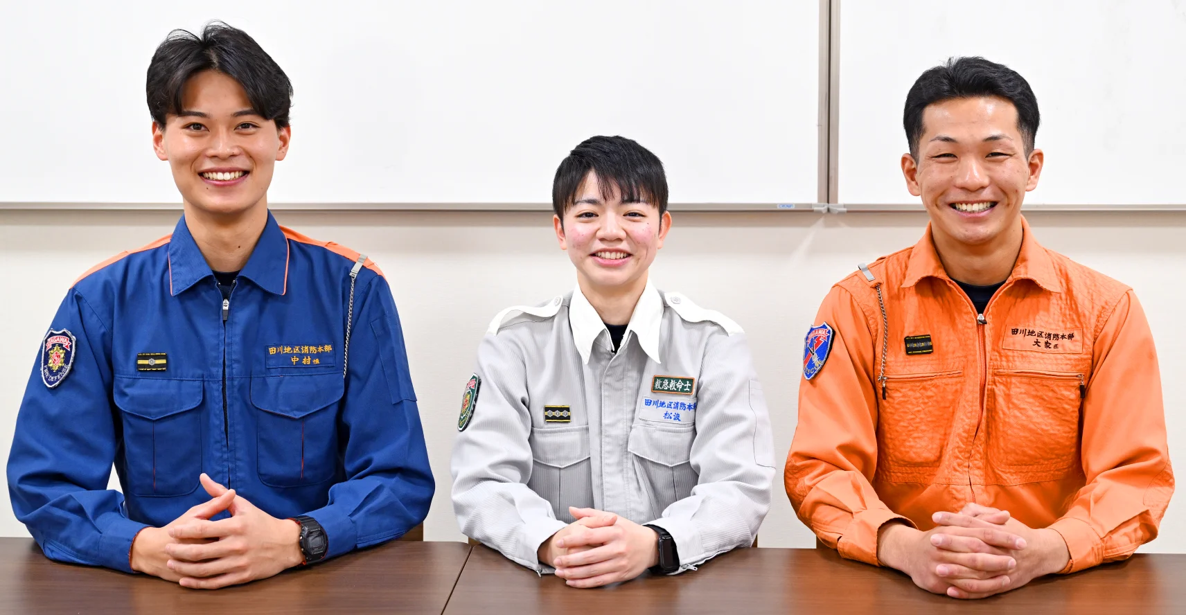 長机の椅子に座った中村さん、松浪さん、大家さんが机の上で手を組み笑顔を浮かべている様子