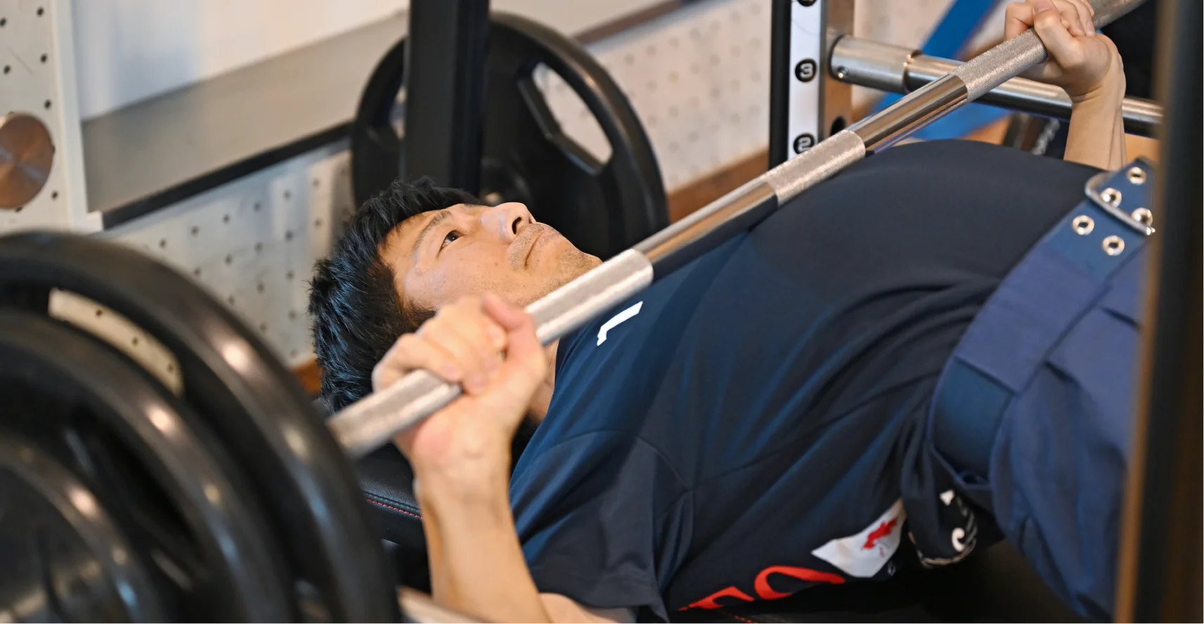 仰向けになった職員が、バーベルを握って持ち上げようとしている様子